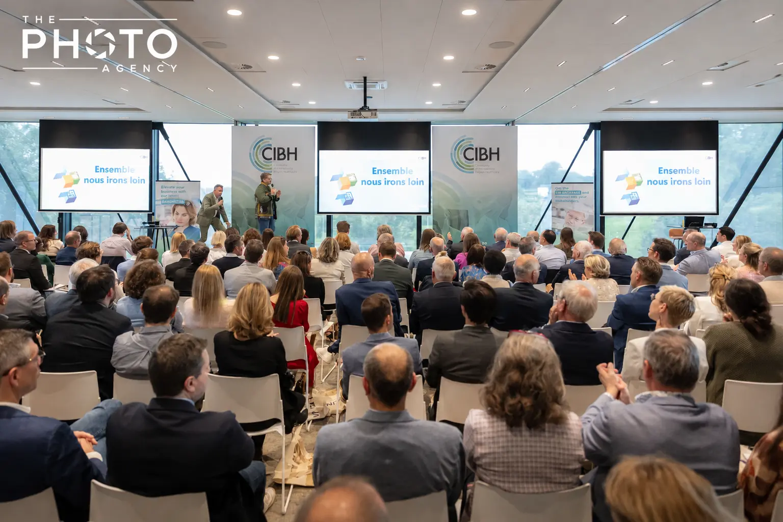 Salle de conférence professionnelle avec une audience attentive, présentateurs sur scène et écrans affichant des logos CIBH